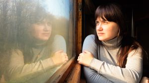 Erotic Charge and the Promise of Another Life - Living From The Heart - Living From The Heart Woman in a light gray turtleneck leans on a train window, gazing outside with her reflection visible on the glass.